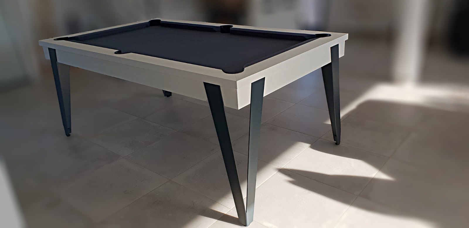 billard moderne d'une finesse extrême rendue possible par une conception autour de pieds métalliques en forme de V ici de couleur noir qui porte l'ensemble du jeu très fin finition blanc ,at avec un tissu de jeu gris anrdoise